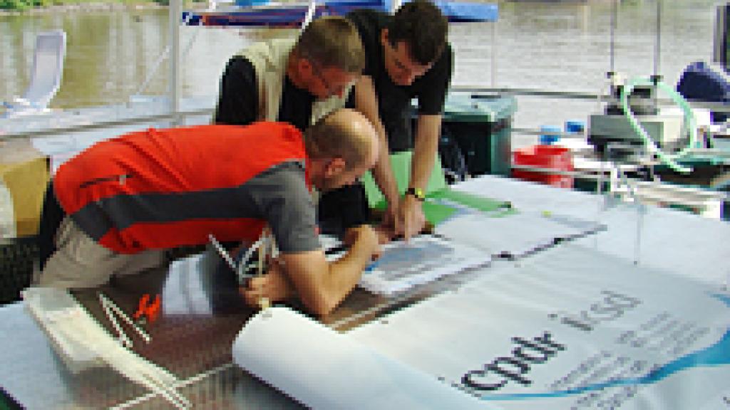 Three men on a boat looking at a map