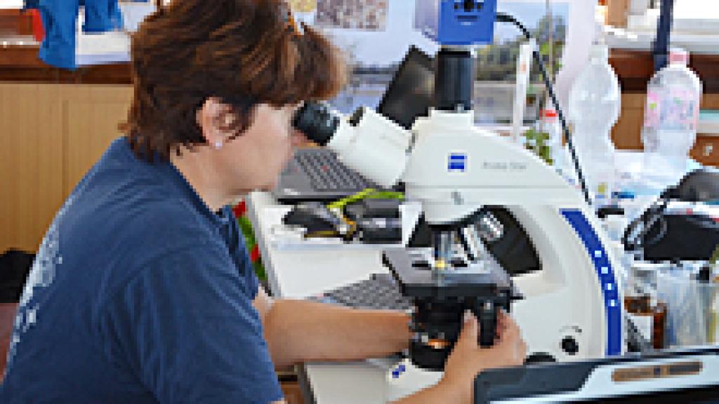 a woman sitting at a desk and looking through a microscope