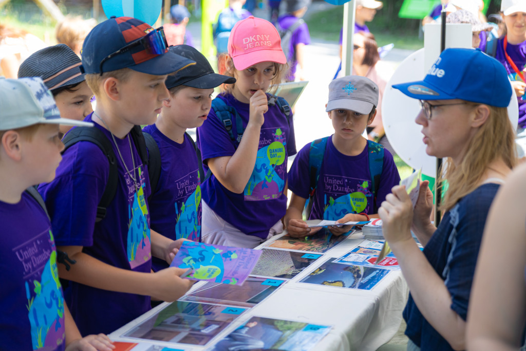 Children wearing Danube Day 2026 tshirts listening to a woman giving explanations 