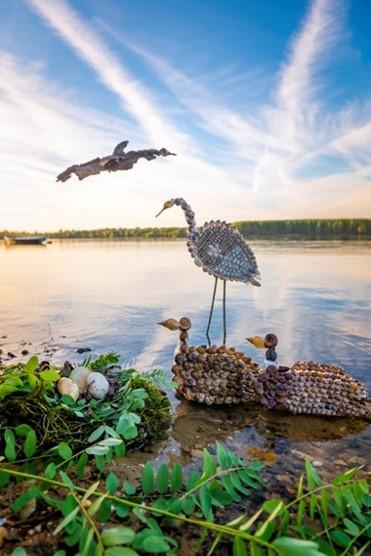 Three bird sculptures on a river bank.