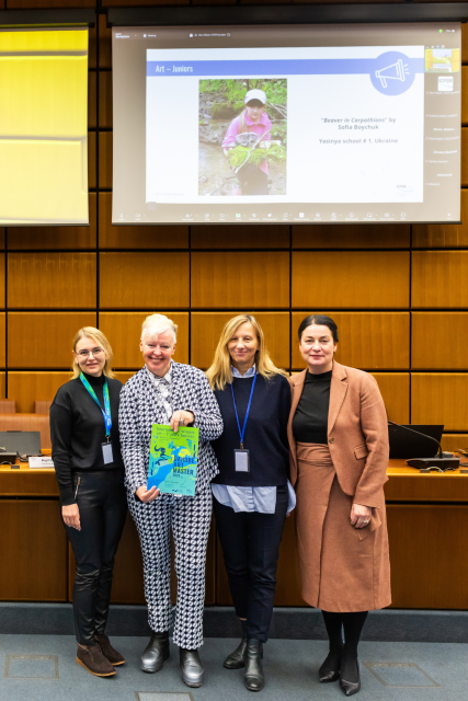 Four people stand together holding a colourful certificate. 