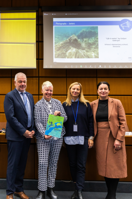 Three women stand with one man holding up a colourful certificate.