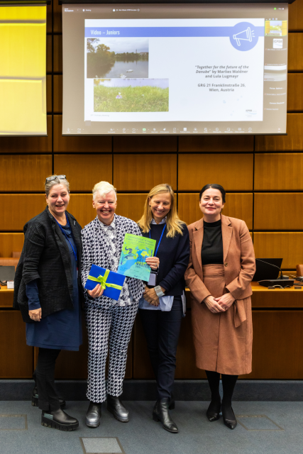Four women stand together holding a colourful certificate. 