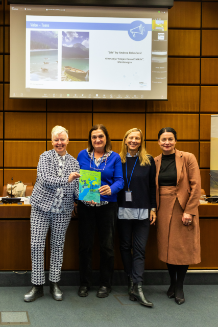 Four women stand together holding a colourful certificate. 