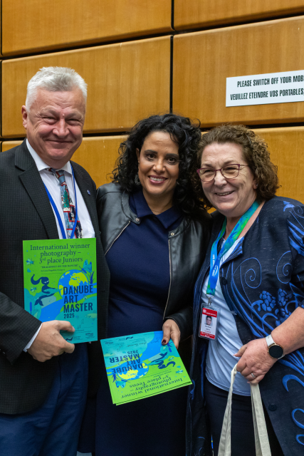 Two women and a man stand together with colourful certificates. 