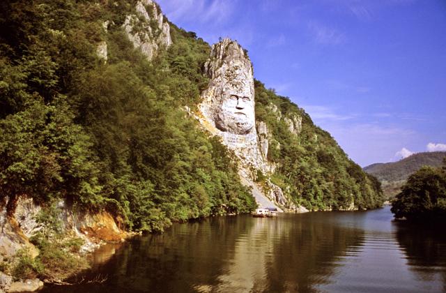 a rock looking like a face surrounded by trees next to a body of water