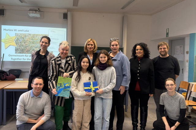 Two young female students holding an award in a classroom. 