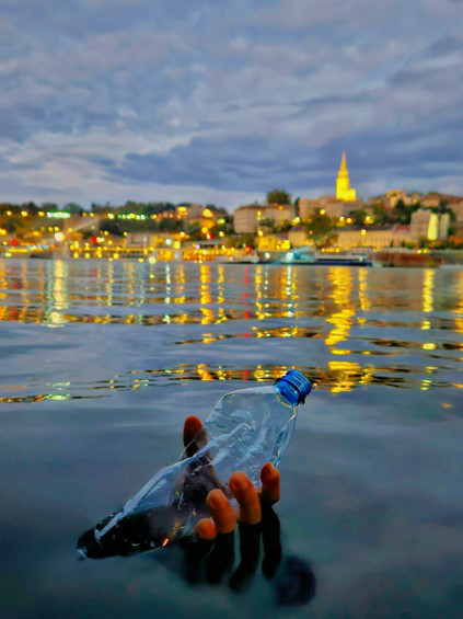 Hand holding a plastic water bottle above surface of water. 